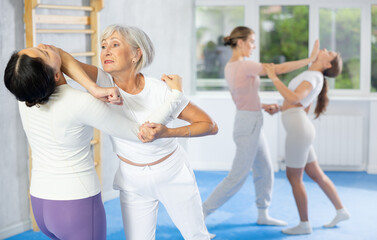 Concentrated elderly woman performing controlled arm lock with precise elbow strike to chin during...
