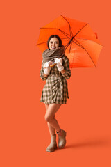 Beautiful young Asian woman in warm scarf with umbrella on orange background