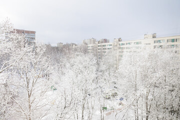 view of snowy city, trees and houses in frosty white snow. climate, winter. New Year and Christmas in city. drifts of white snow and ice. snow removal equipment. winter nature