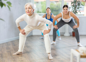 Obraz premium Sporty motivated young elderly women warming up with energetic dances before strength training in gym studio