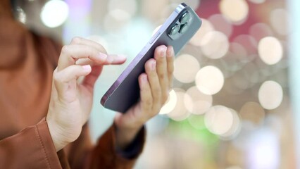 Сlose up female hand using smartphone communication with light bokeh standing indoor shopping center mall. Woman use online store for Christmas holiday discount, sale promotions using a mobile phone
