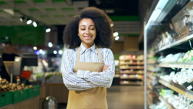 Portrait of a saleswoman female worker in a supermarket looking at camera and smiling. African american black woman employee clerk in apron in grocery store Happy Positive greengrocer girl in market