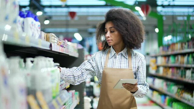 African american black woman, employee clerk working on tablet, checking condition of product in store market standing near cosmetics shelves Manager writes products list inventory in supermarket