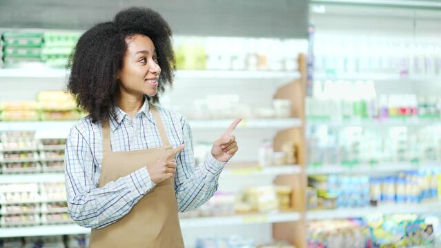 A seller in a grocery store points with a finger to an empty space for advertising. Copy space African American female employee clerk worker or small business owner in a supermarket looking at camera