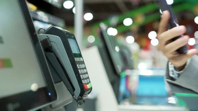 Close up Woman At Counter Buy electronic payment supermarket smartphone close-up Female hand with a mobile phone in hands pay paid for purchases in stores Contactless NFC Terminal Closeup card reader