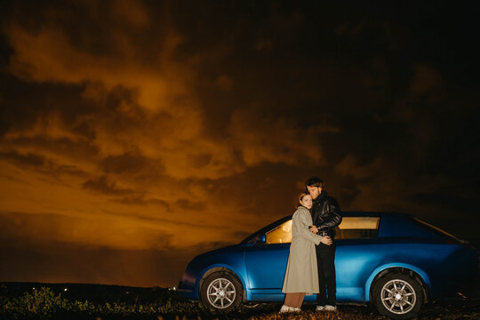 couple in love under the night cloudy sky with a car on a trip.