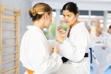 Concentrated young Asian woman in kimono and black belt honing punching techniques during training sparring with female opponent at karate workout..