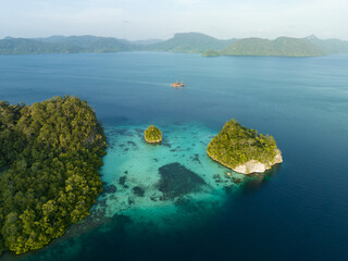 Limestone islands, covered by tropical vegetation, are fringed by coral reefs in the calm Alyui...