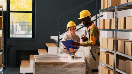 Warehouse team review shipping list in storage room, looking at stock inventory and supply chain before retail distribution. Young employees checking merchandise orders in stockroom.