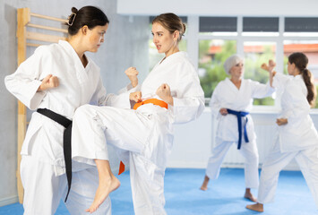 Determined motivated young woman working on knee strikes and blocks in training fight during group martial arts workout..
