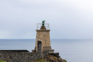 Fototapeta na wymiar a stone lighthouse with a green statue on top, overlooking the calm ocean under an overcast sky