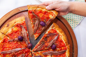 Taking slice of pizza top view with close up with aliche and tomatoes