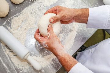 Chef hand working on dough top view close up with flour background
