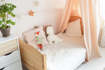 A cozy and bright children's bed with a canopy has cute soft toys on the bed. There is a green plant next to the bed. light background
