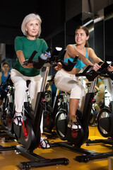Fototapeta na wymiar Young and mature women doing cardio workout at gym, training together on exercise bikes