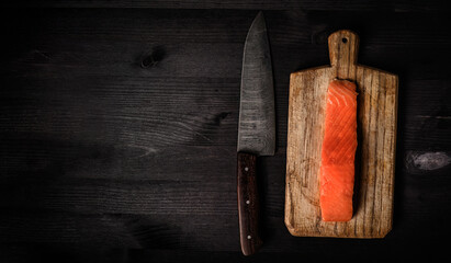 fillet of raw salmon red fish on a cutting board with a big kitchen knife, top view with a copy...