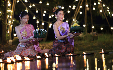 Two beautiful Asian young females in Thai ancient dressing hold and make a wish with Kratong flower...