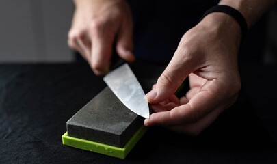 Man Uses Natural Sharpening Whetstone To Sharpen Big Kitchen Knife Against Black Background