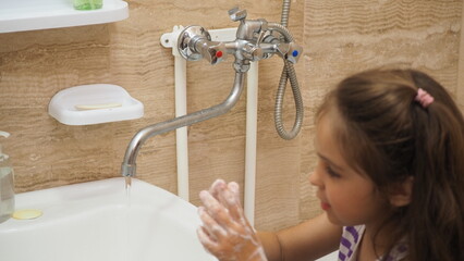 a little cute girl with long dark hair washing in the bathroom. close up hands of children or...