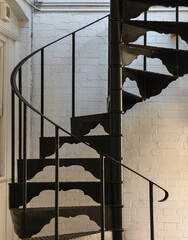Vertical view of Black metal spiral staircase pattern with iron railing lead from the ground floor to the upper floor on the side of white brick wall. Ladder decoration exterior, Copy space, Selective