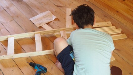 Young teenager boy assembling furniture at home. boy using a screwdriver tool assembles parts of...