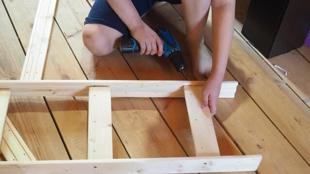 Young teenager boy assembling furniture at home. boy using a screwdriver tool assembles parts of wooden furniture, shelving. interior, cozy home, help for parents