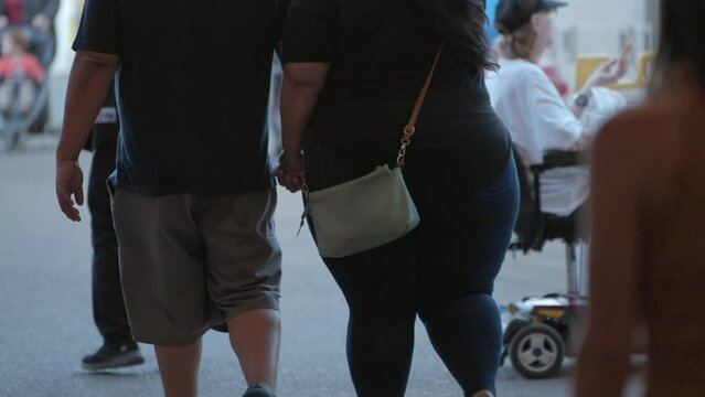 This video shows a close up, rear view of a fat obese couple walking by in slow motion.