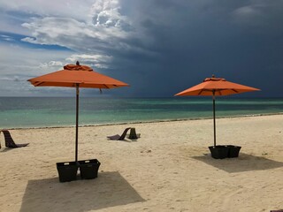 Sandy beach with a row of orange umbrellas and beach chairs near a tranquil body of water