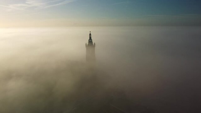 Drone footage of St. Christopher Cathedral bell tower covered with fog at sunrise in Roermond