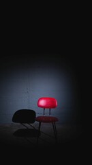 Red chair stands illuminated in a spotlight, casting an empty silhouette in a dark space