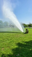 Firefighter in full protective gear spraying a powerful fire hose sitting on a grassy yard