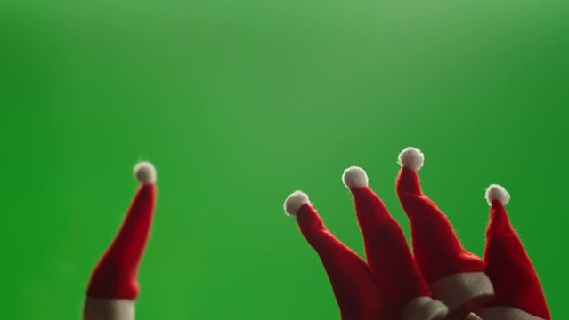Little Christmas hats on green screen chroma key background close-up. Elfs, dwarfs in red hats walking at home near christmas tree. Vibes of winter holidays,2024, 2025
