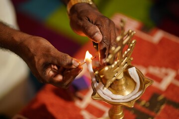 Closeup of a woman's hands lighting a candle in a brass Christian cross lamp