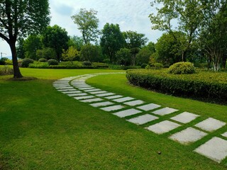 grass pathway surrounded by greenery in park of green trees and shrubs