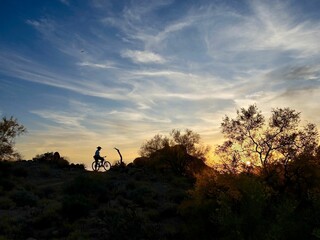 Silhouetted figure enjoying an evening bike ride on a hilltop at sunset.