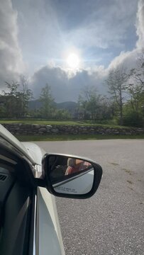 Vertical side shot of a car driving on a road with fields and rees with dramatic shiny sky