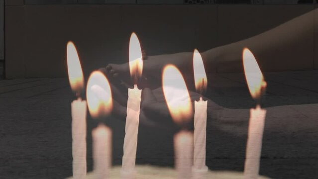 Composite video of candles blowing off over woman hands with rosary praying against people walking