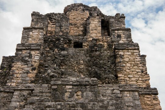 Image of the ancient Mayan ruins taken from a low angle, set against a cloudy sky