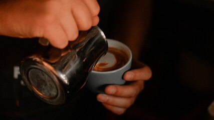 Close-up of a human hand pouring a hot beverage from a mug into a white cup