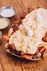 Closeup shot of a dish with french fries, sausages topped with cheese and corn on a wooden table.
