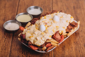 Closeup shot of a dish with french fries, sausages topped with cheese and corn on a wooden table.