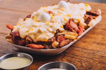 Closeup shot of a dish with french fries, sausages topped with cheese and corn on a wooden table.