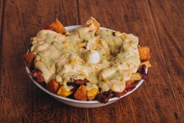 Closeup shot of a dish with french fries, sausages topped with cheese and corn on a wooden table.