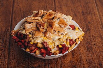 Closeup shot of a dish with french fries, sausages topped with cheese and corn on a wooden table.