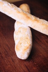 Vertical shot of two freshly baked loaves of bread placed side by side on a wooden table