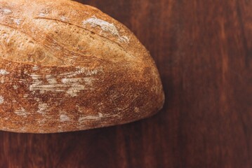 Freshly-baked bread resting on a wooden table top, with a light dusting of flour