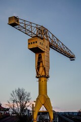 Vertical shot of a large yellow construction crane in a field in the evening