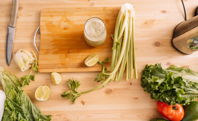 Prepared celery smoothie on a wooden table with fresh vegetables on it.