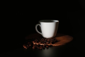 White ceramic cup on a wooden board with coffee beans on a dark background