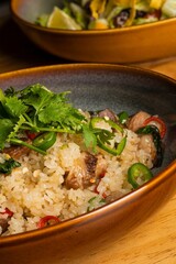 Vertical closeup of a bowl of rice with greens on a wooden table